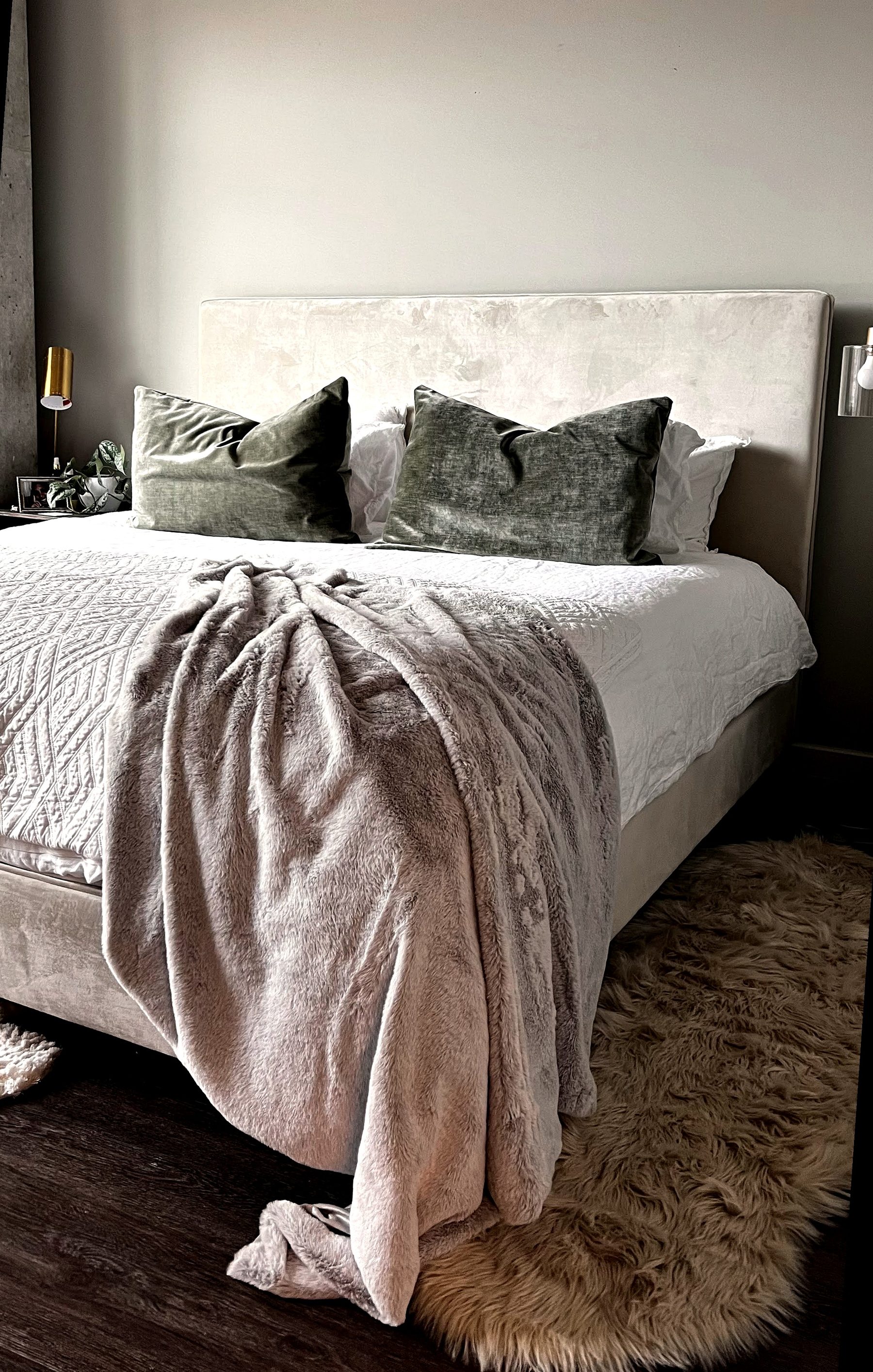 Bed styled with olive velvet pillows and a faux fur throw draped over a textured white coverlet