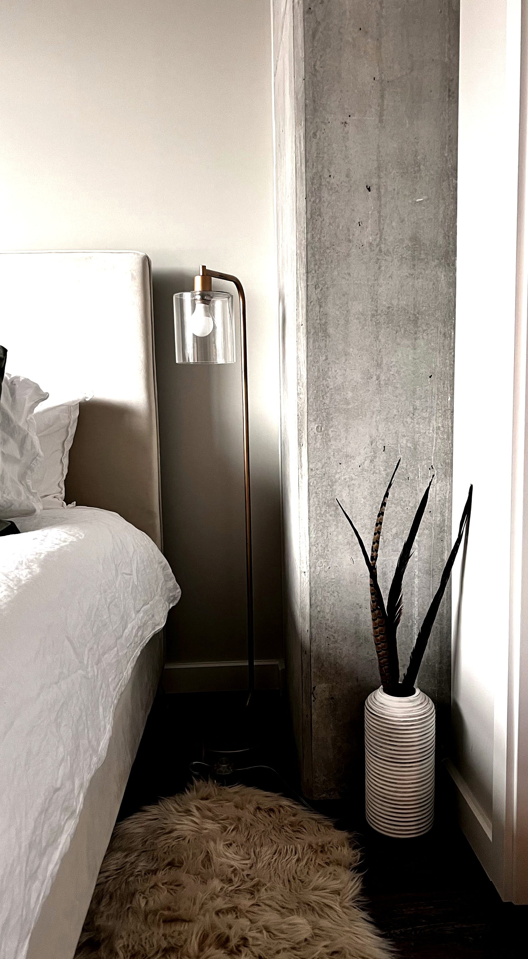 Floor lamp and feather-filled vase in a corner beside a concrete pillar