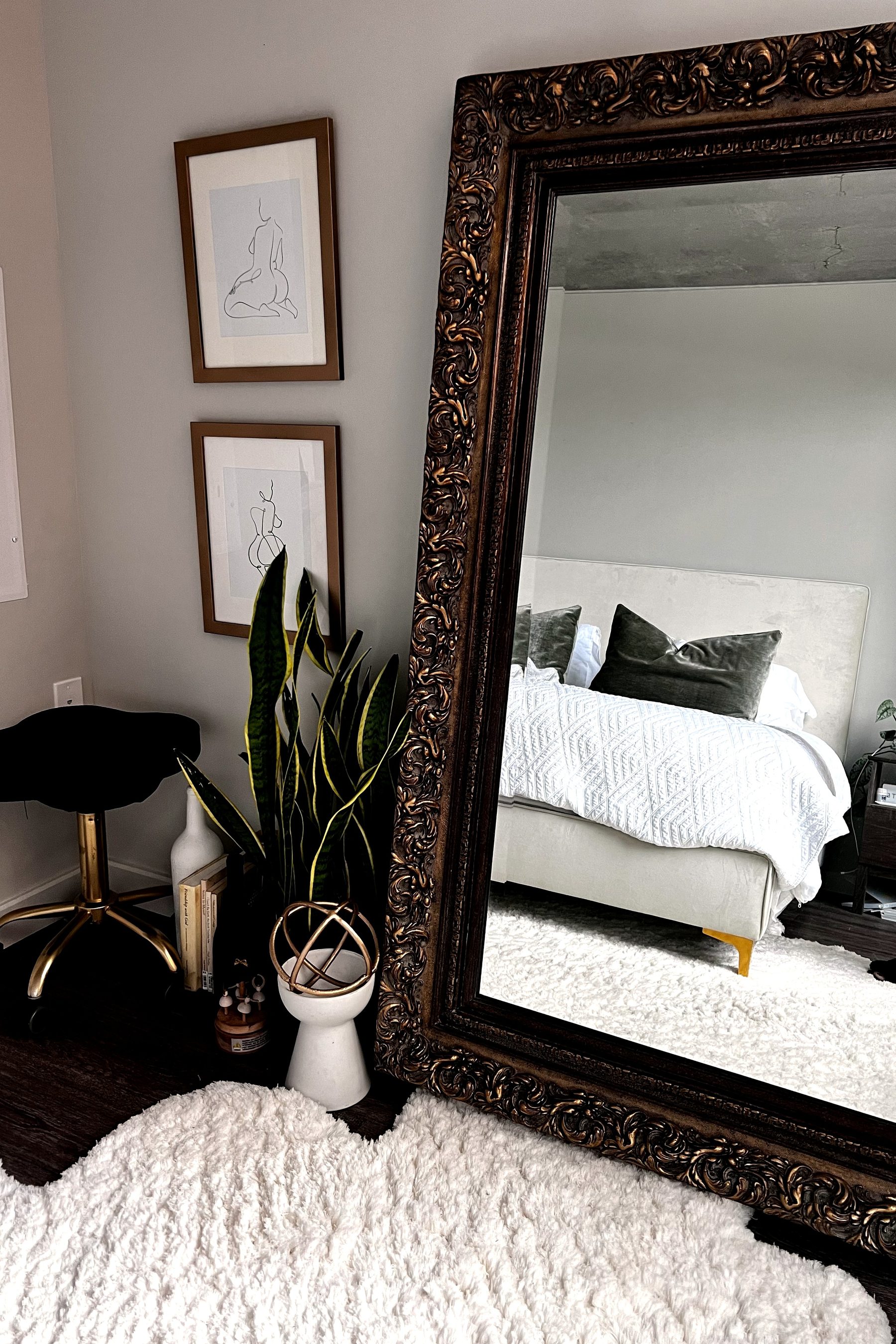 Full bedroom reflected in an ornate antique mirror, with green velvet pillows and a textured white coverlet