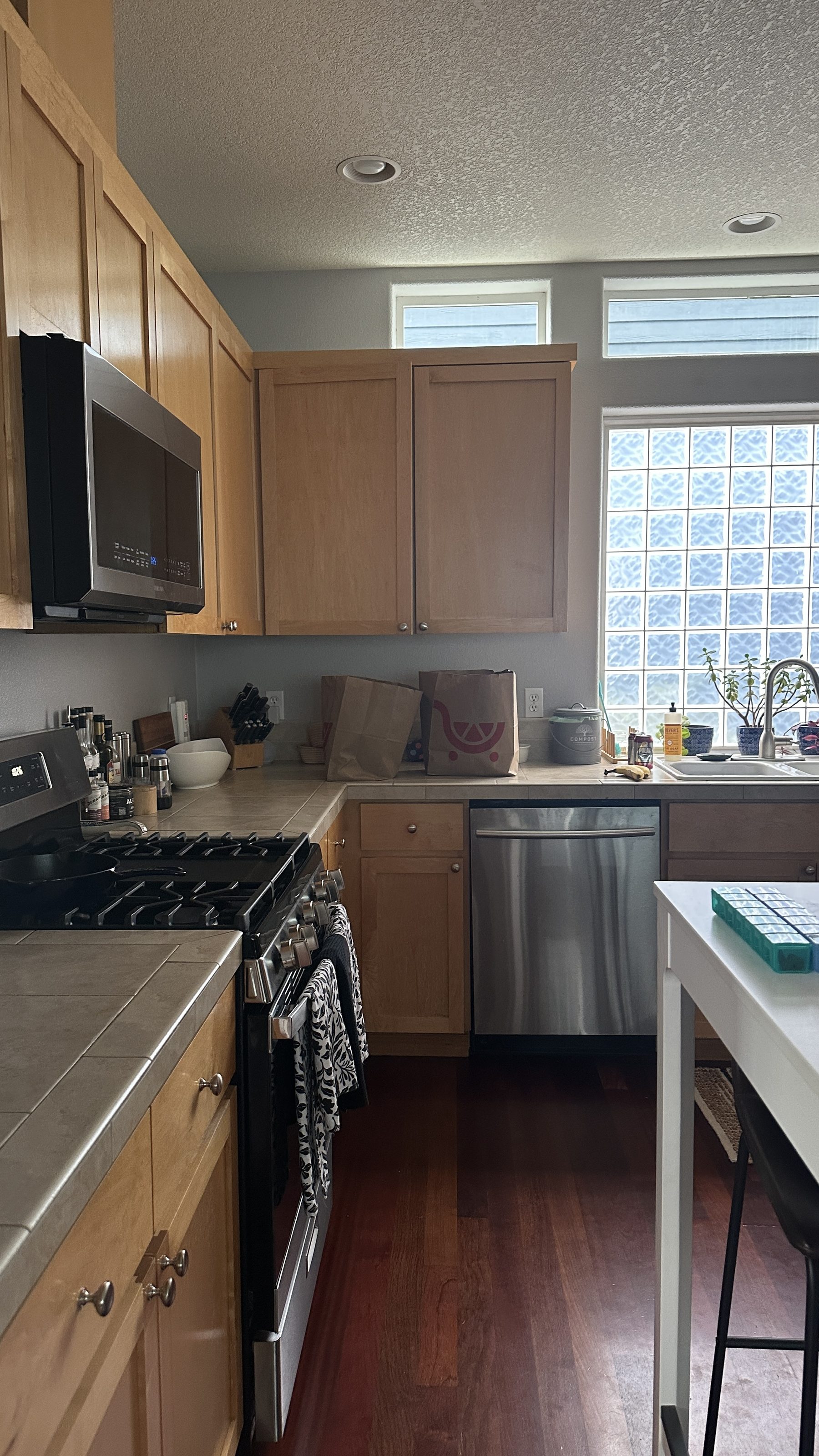Existing kitchen with honey oak cabinets, tile countertops, and glass block window before renovation
