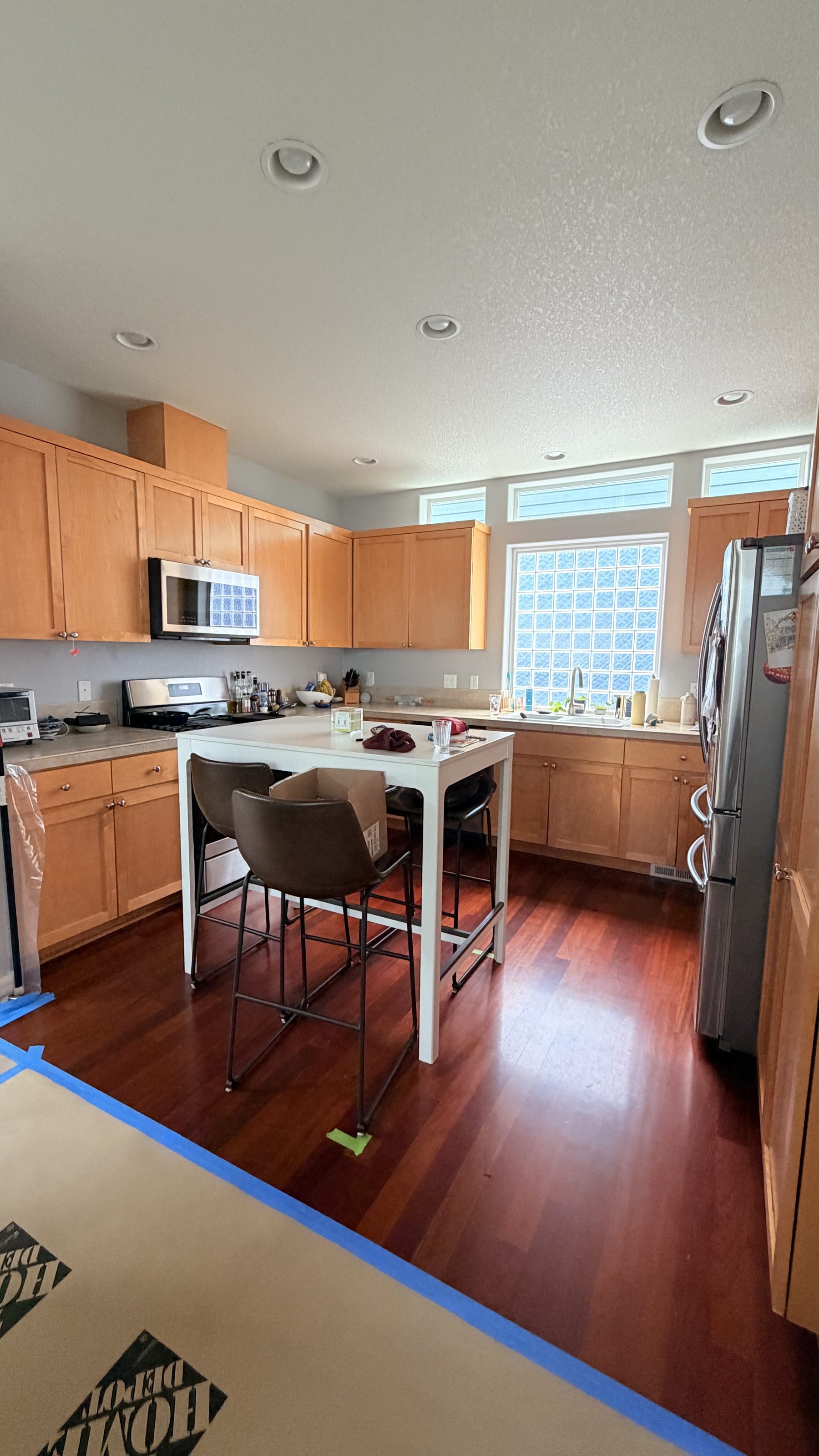 Wider view of the kitchen with protective floor covering and painter's tape during active renovation