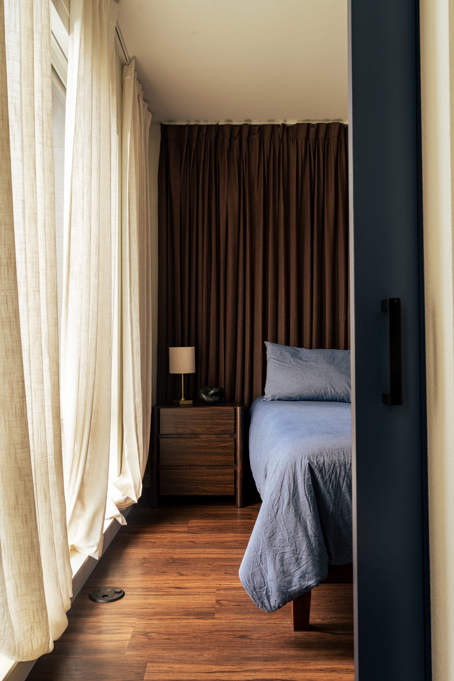 Bedroom nook with walnut nightstand, brass lamp, and blue linen bedding