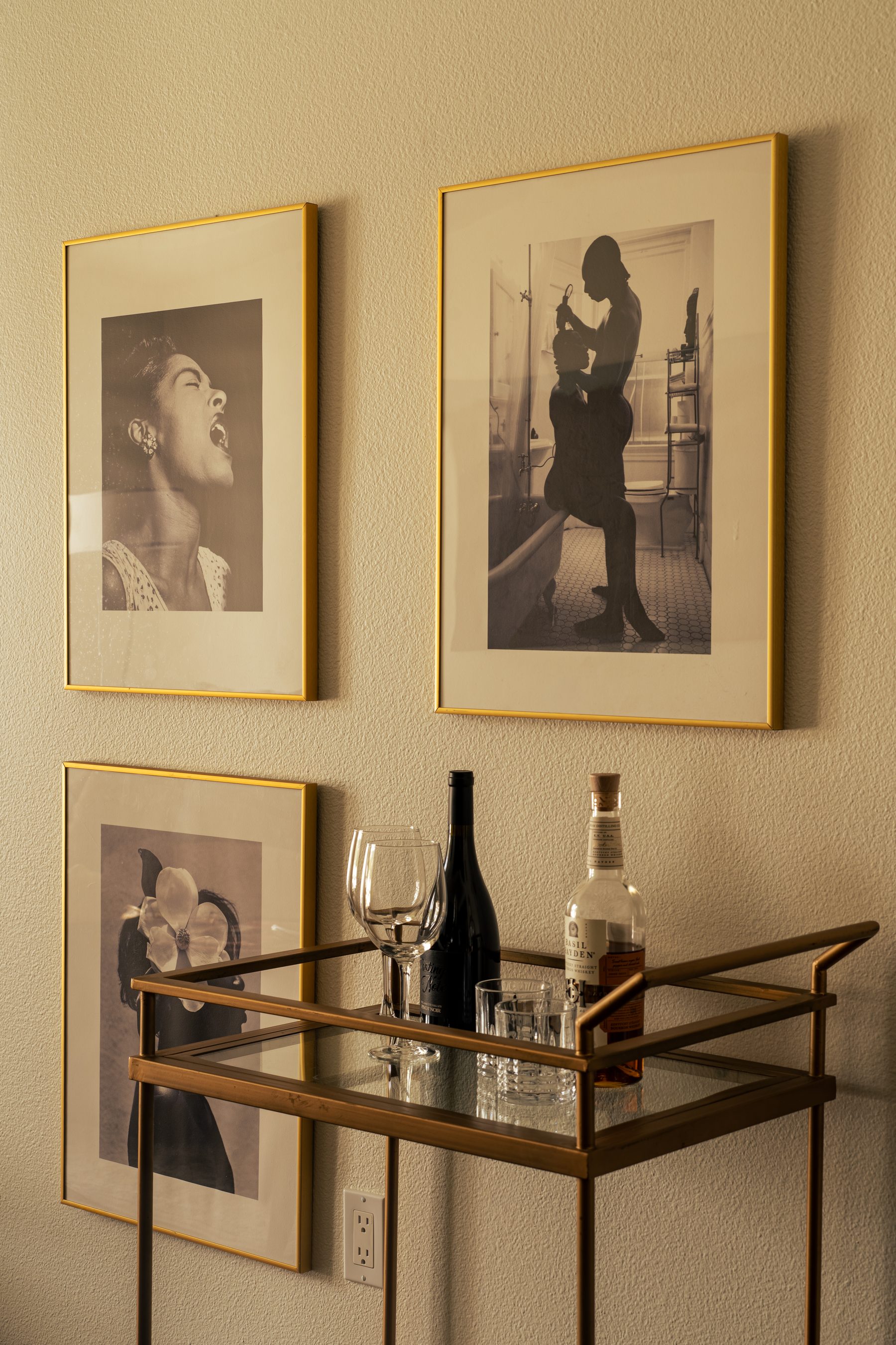 Gallery wall of three sepia portrait photographs beside a gold bar cart