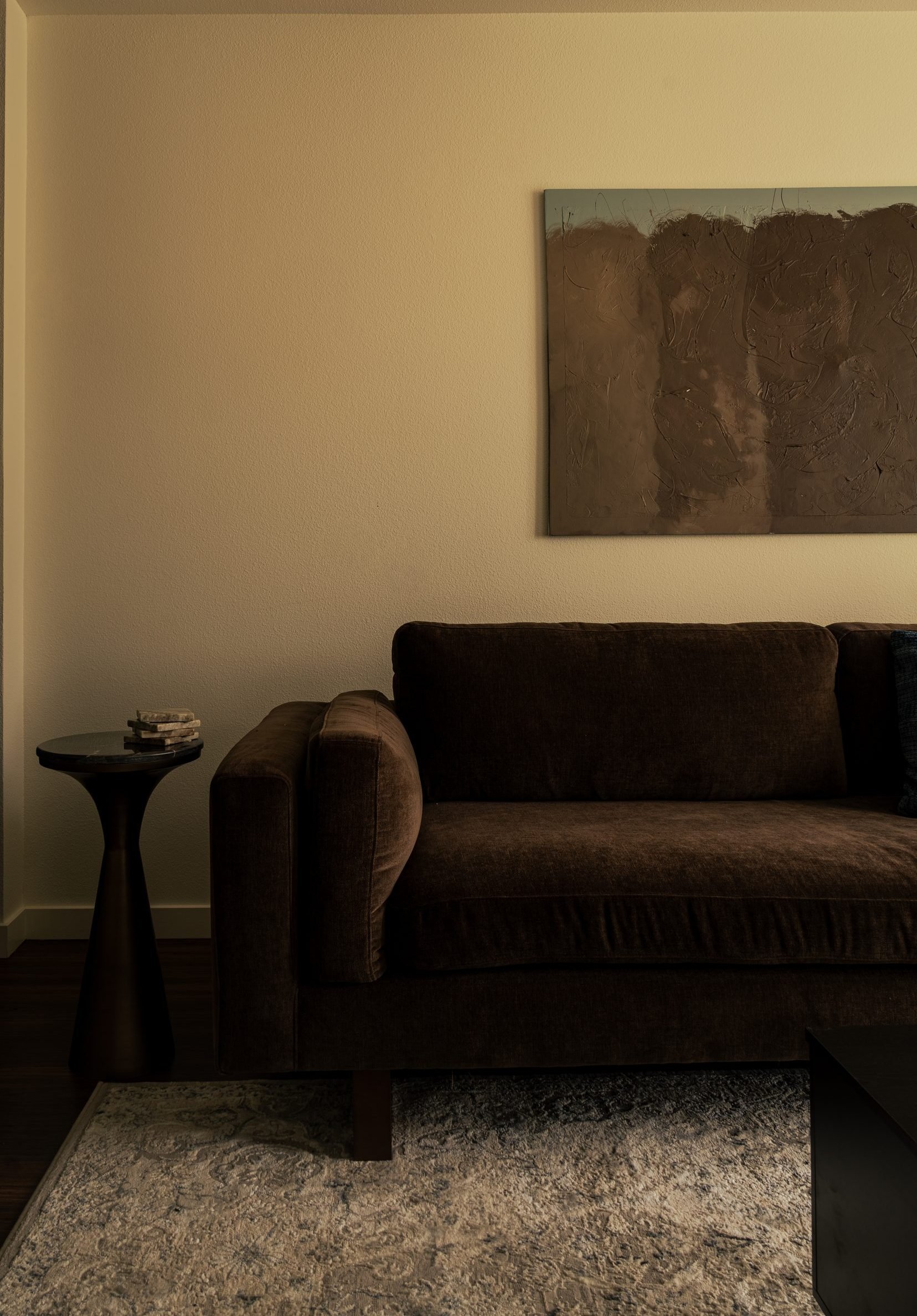 Living room with dark walls, textured abstract art, and a walnut side table